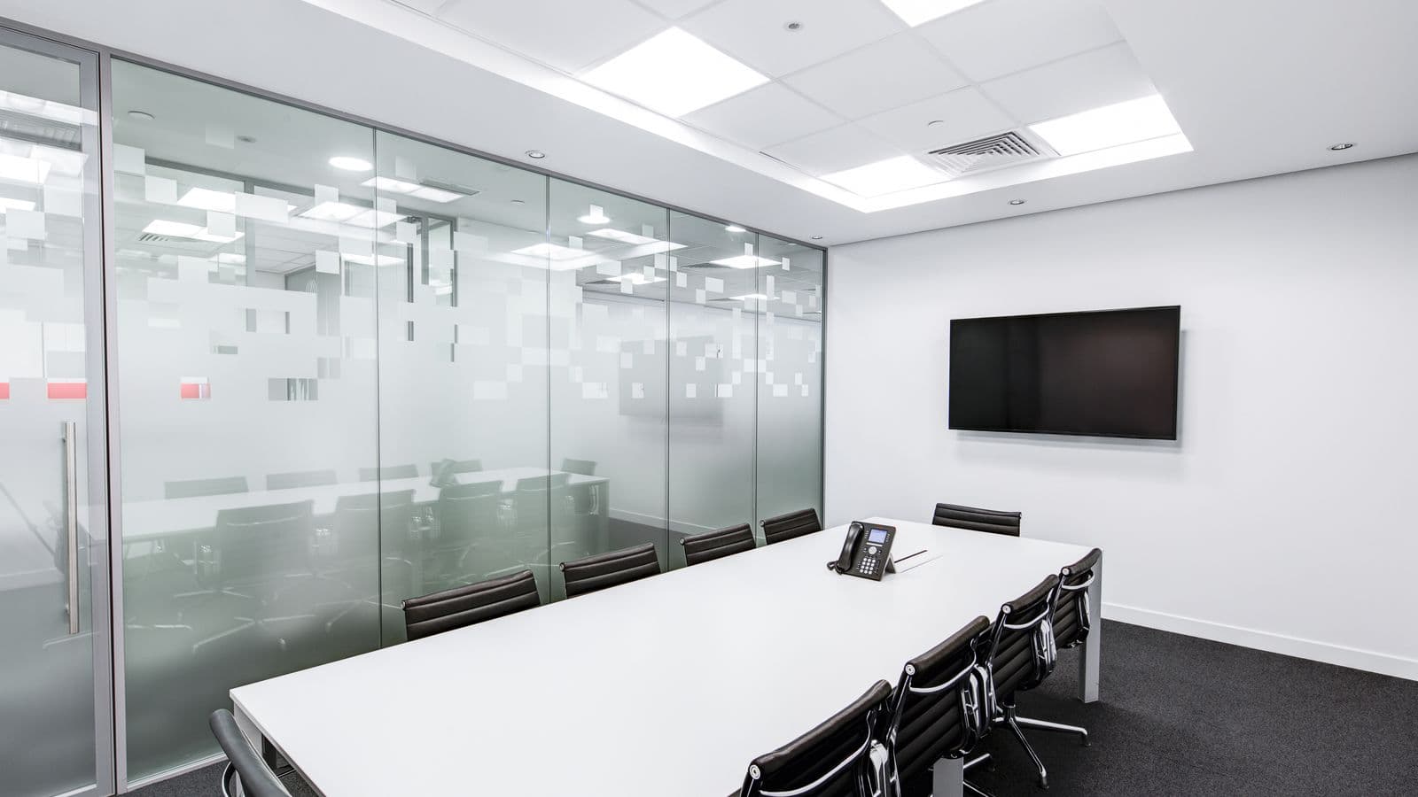 Empty corporate boardroom with a white table, black chairs and a blank wall screen under fluorescent panels